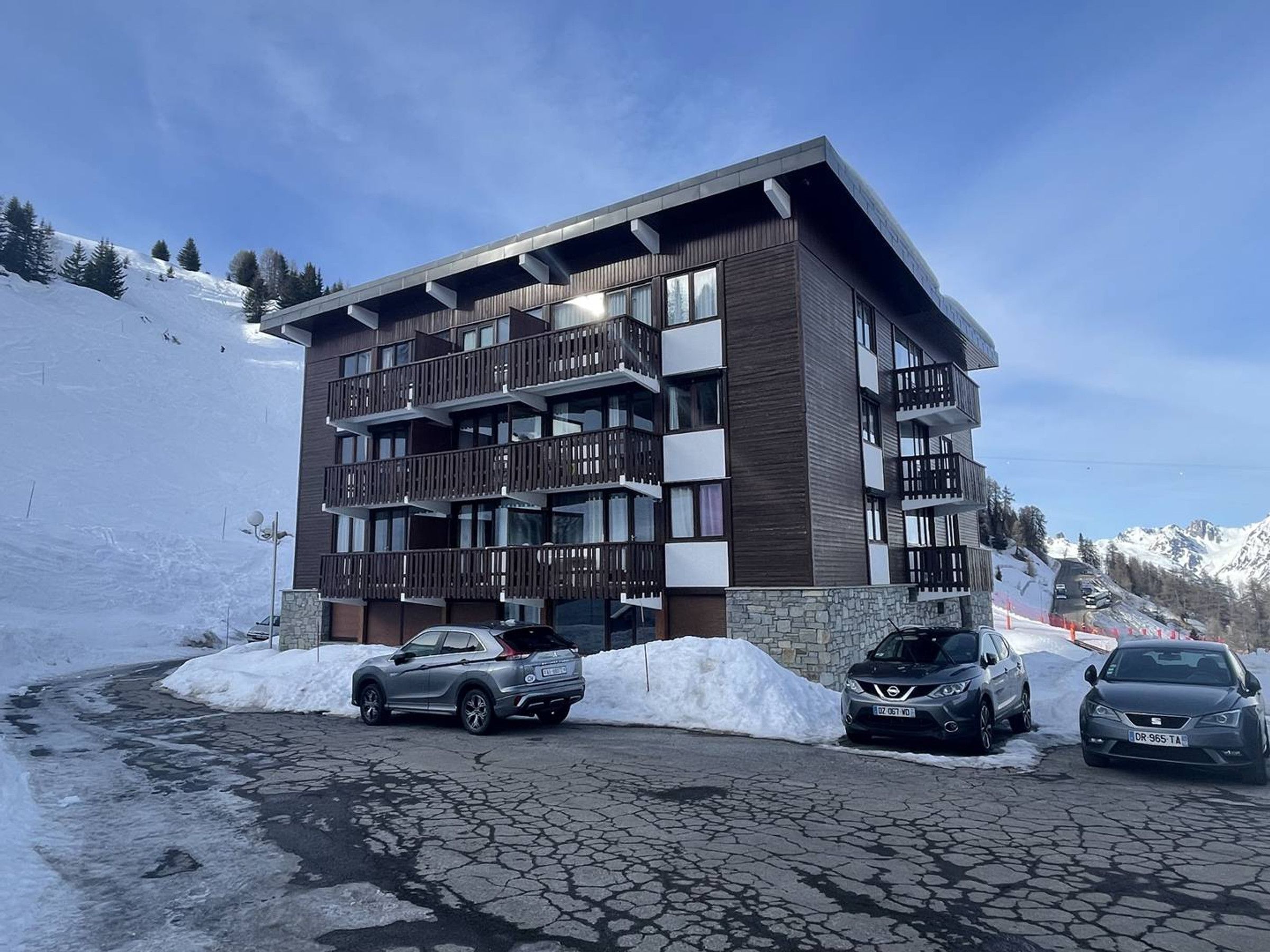 Un hotel de varios pisos con balcones, fachada de piedra y un estacionamiento con automóviles.
