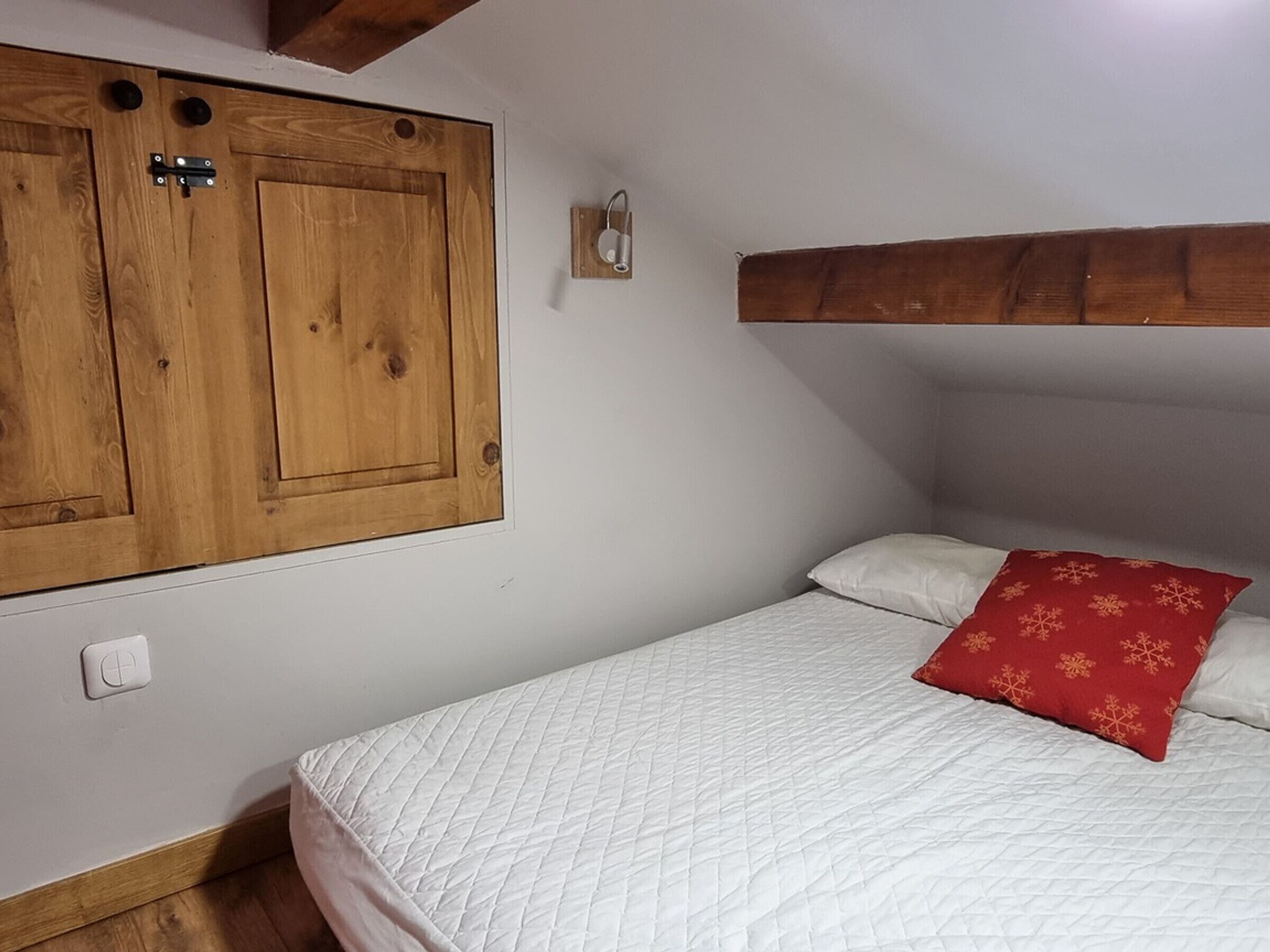 A bedroom with a bed, a wooden wardrobe, and a small wall-mounted light.