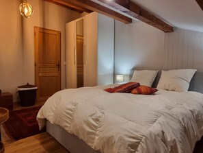 A bedroom with a large bed, wooden beams, a wardrobe, and a small bedside table.