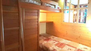 Un lit superposé avec une échelle en bois, une fenêtre avec des rideaux et une couvre-lit matelassé.