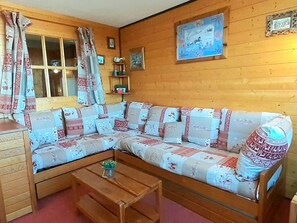 Ein gemütliches Zimmer mit einer Holzcouch, einem Holztisch und einem Fenster mit Vorhängen.