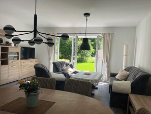 A modern living room with a dining area, a sofa, a coffee table, and a TV. - House Kanalliebe (Schülp b. Rendsburg)