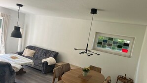 Een moderne woonkamer met een bank, een eettafel met stoelen, een hanglamp en een raam met uitzicht.