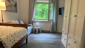 Een slaapkamer met een bed, een klein tafeltje, een radiator, een raam met gordijnen en een kledingkast.