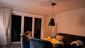 Een woonkamer met een bank, een tafel met kaarsen en een plafondlamp.