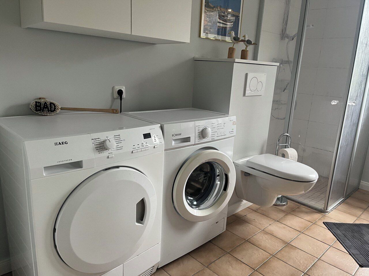 Un espace buanderie compact comprenant un lave-linge et un sèche-linge à chargement frontal, des toilettes et une douche.