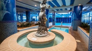 Une statue se trouve dans un espace piscine dont les murs sont recouverts de carreaux et dont le plafond est orné de rayures bleues et blanches.