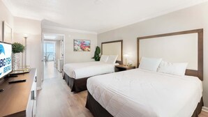 Une chambre d’hôtel avec deux lits, un bureau avec un ordinateur, une télévision et une vue sur le balcon.