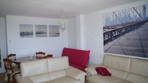 A living room with a dining area, a chandelier, and a large cityscape painting on the wall.