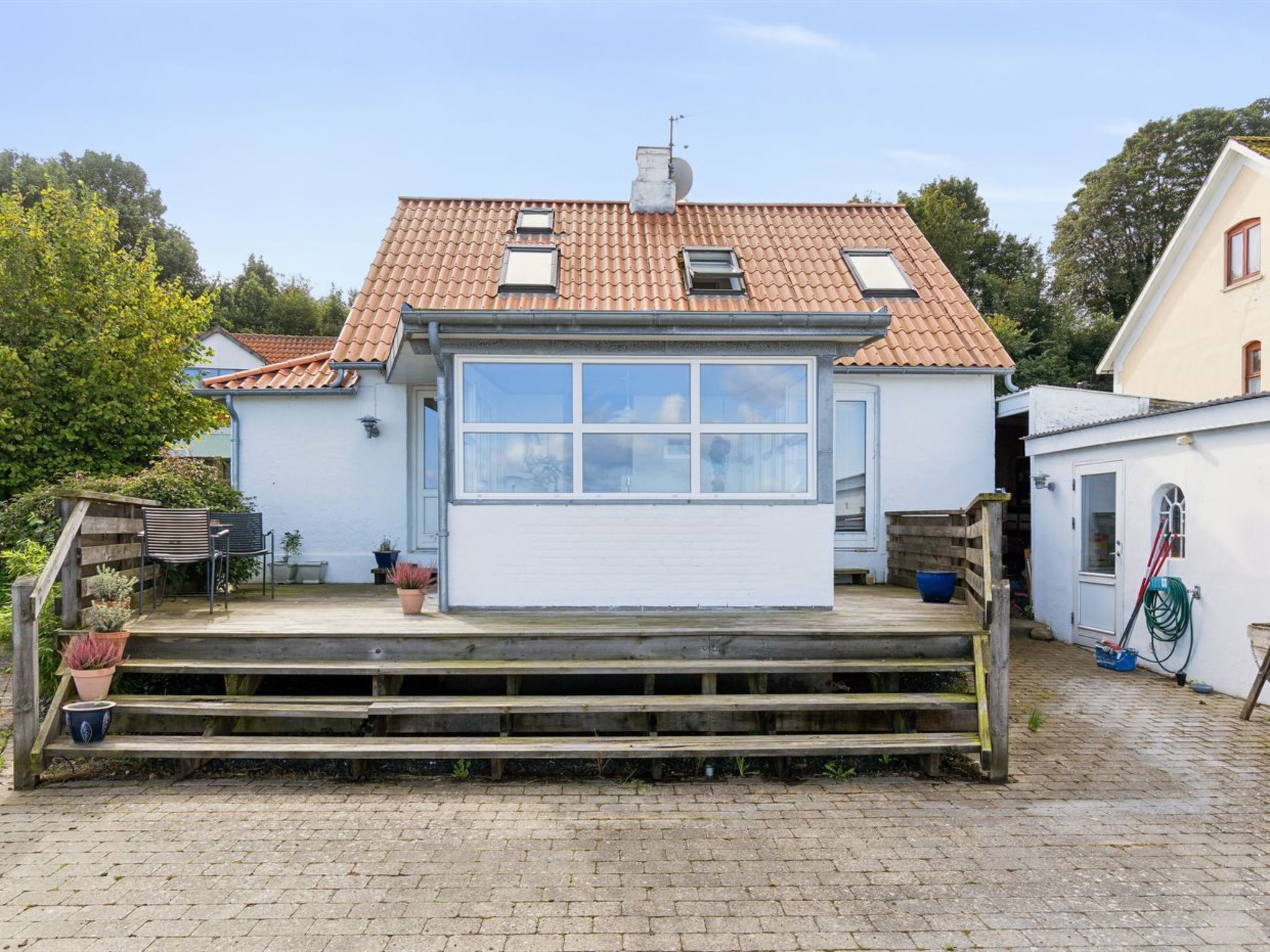 Ett envåningshus med ett tegeltak, en veranda med trappsteg och en liten trädgårdsyta med krukväxter.