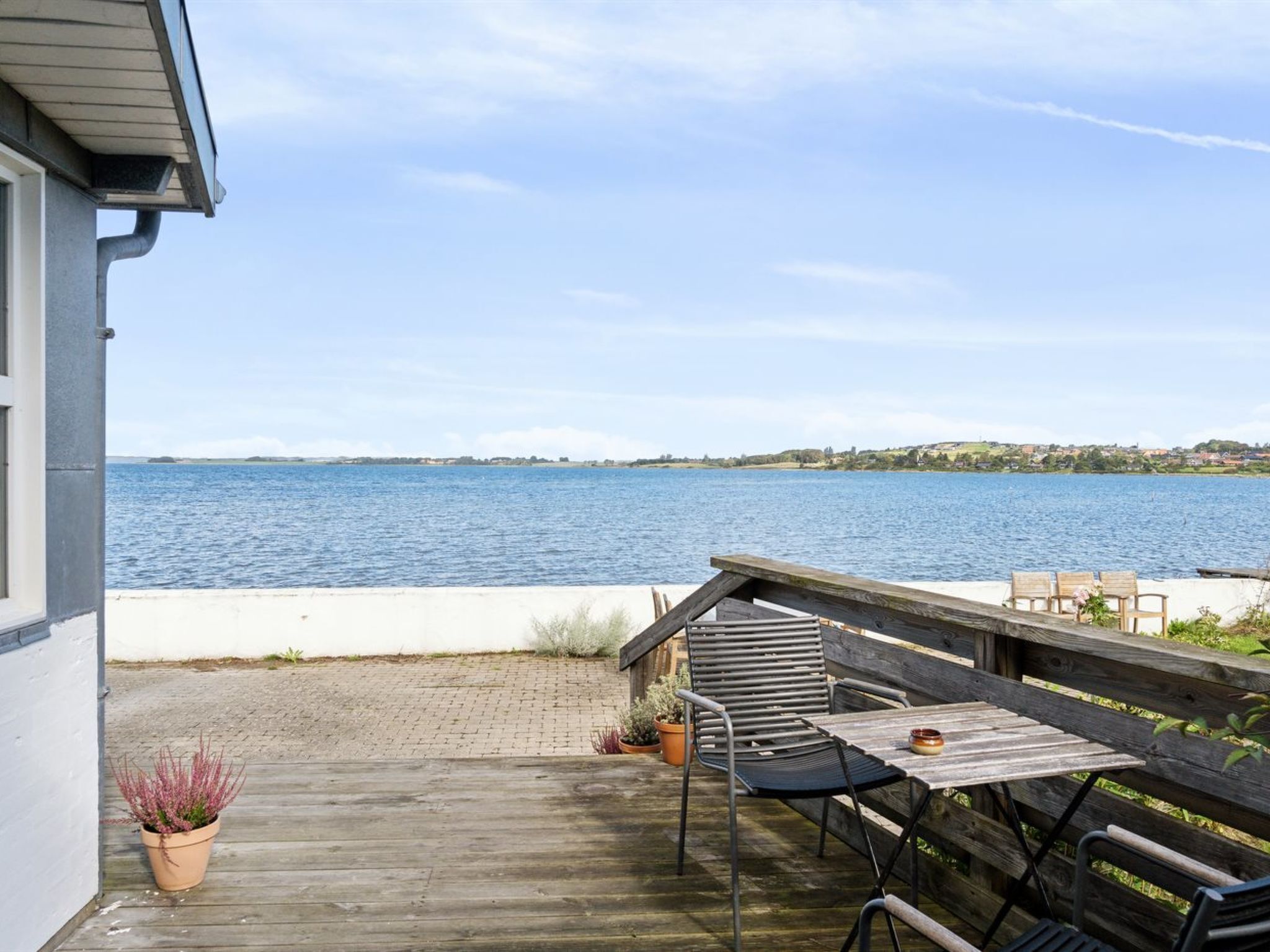 Een houten terras met een tafel en stoelen, uitkijkend op een waterpartij.
