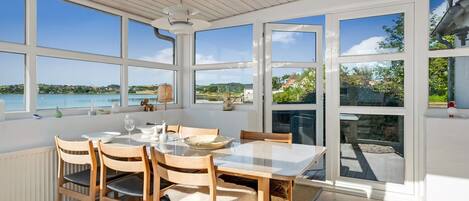 A dining area with a table and chairs, large windows, and a view of a body of water.