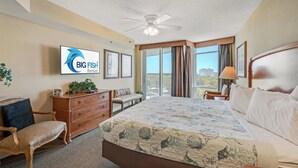 Habitación de hotel con cama, cómoda, silla, escritorio, ventilador de techo y un ventanal con cortinas.