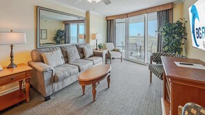 Habitación de hotel con una cama grande, un escritorio, una silla, un sofá, un ventilador de techo y un amplio ventanal con vistas a la ciudad.
