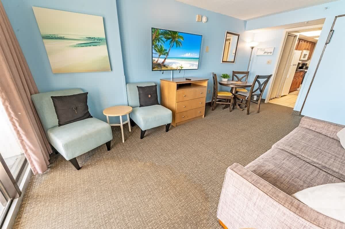 A living room with a TV, a small table, two chairs, a sofa, and a wooden cabinet.