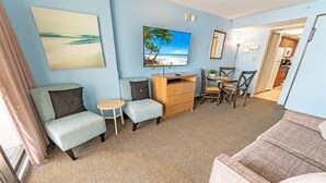 A living room with a TV, a small table, two chairs, a sofa, and a wooden cabinet. - NEW, Landmark Direct Oceanfront View - Pools 1BR! (Myrtle Beach)