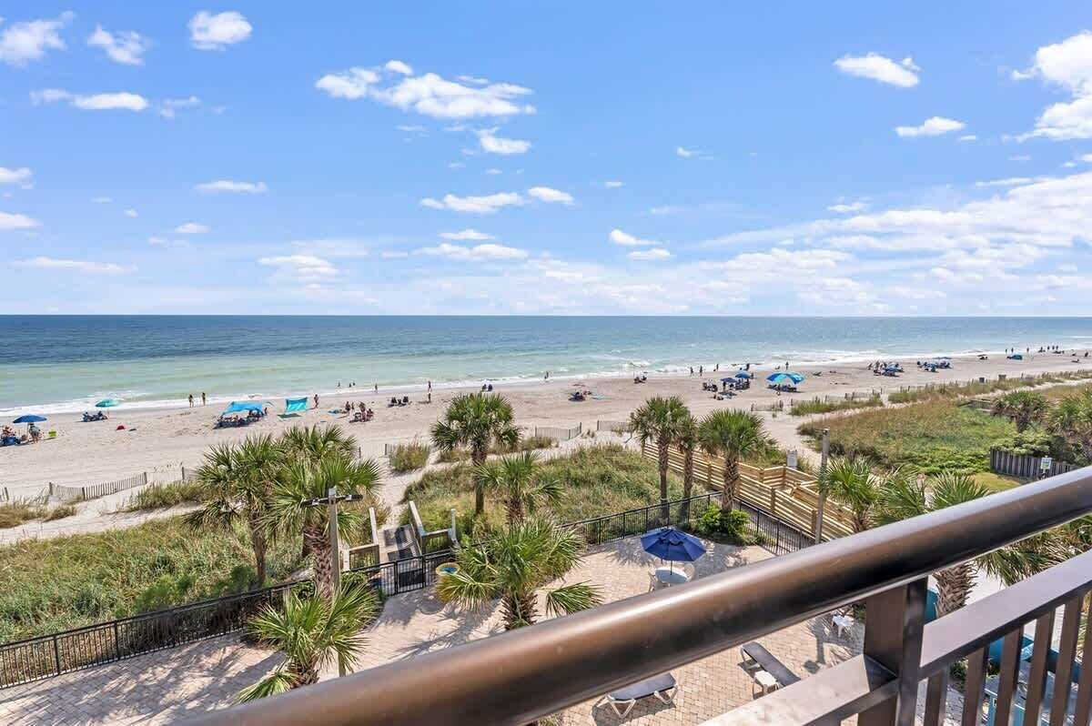 A beach with palm trees, umbrellas, and a clear sky.