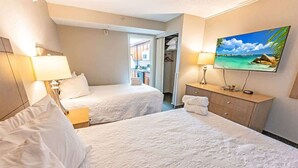 A hotel room with two beds, a TV, a desk, and a view of the outside. - NEW, Landmark Direct Oceanfront View - Pools 1BR! (Myrtle Beach)