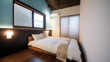 A bedroom with a bed, a window, an air conditioning unit, and a wall-mounted light fixture.