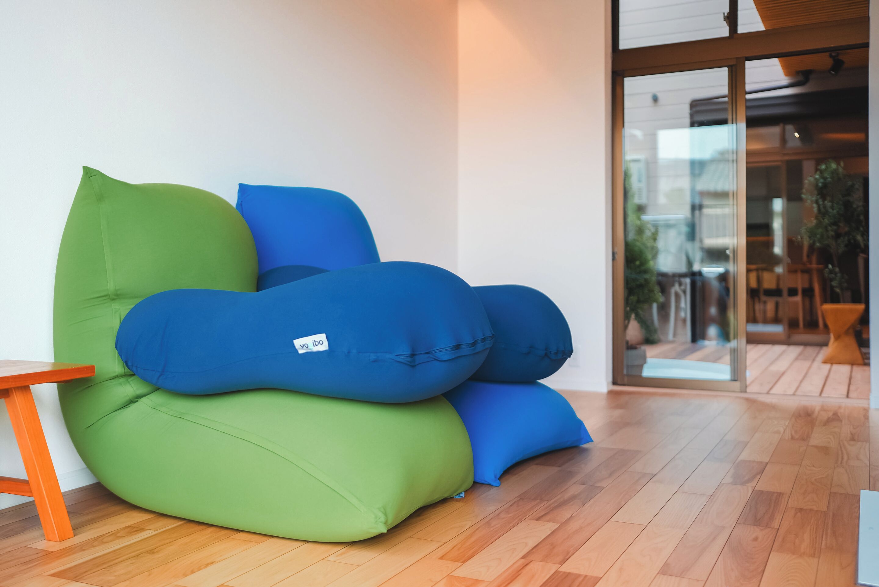 A green and blue bean bag chair in a room with wooden flooring and a glass door leading outside.