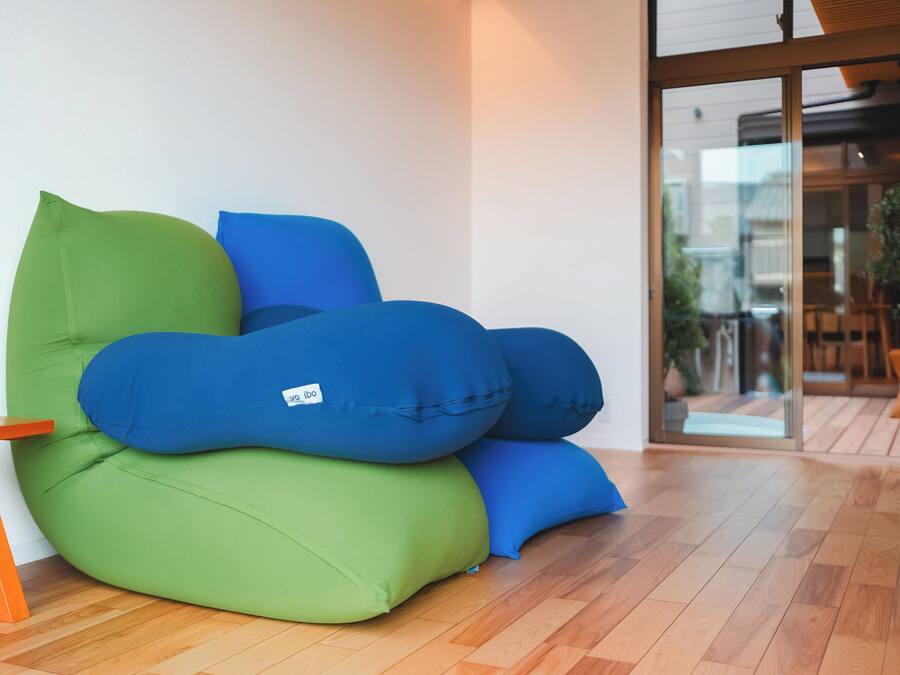 A green and blue bean bag chair in a room with wooden flooring and a glass door leading outside.