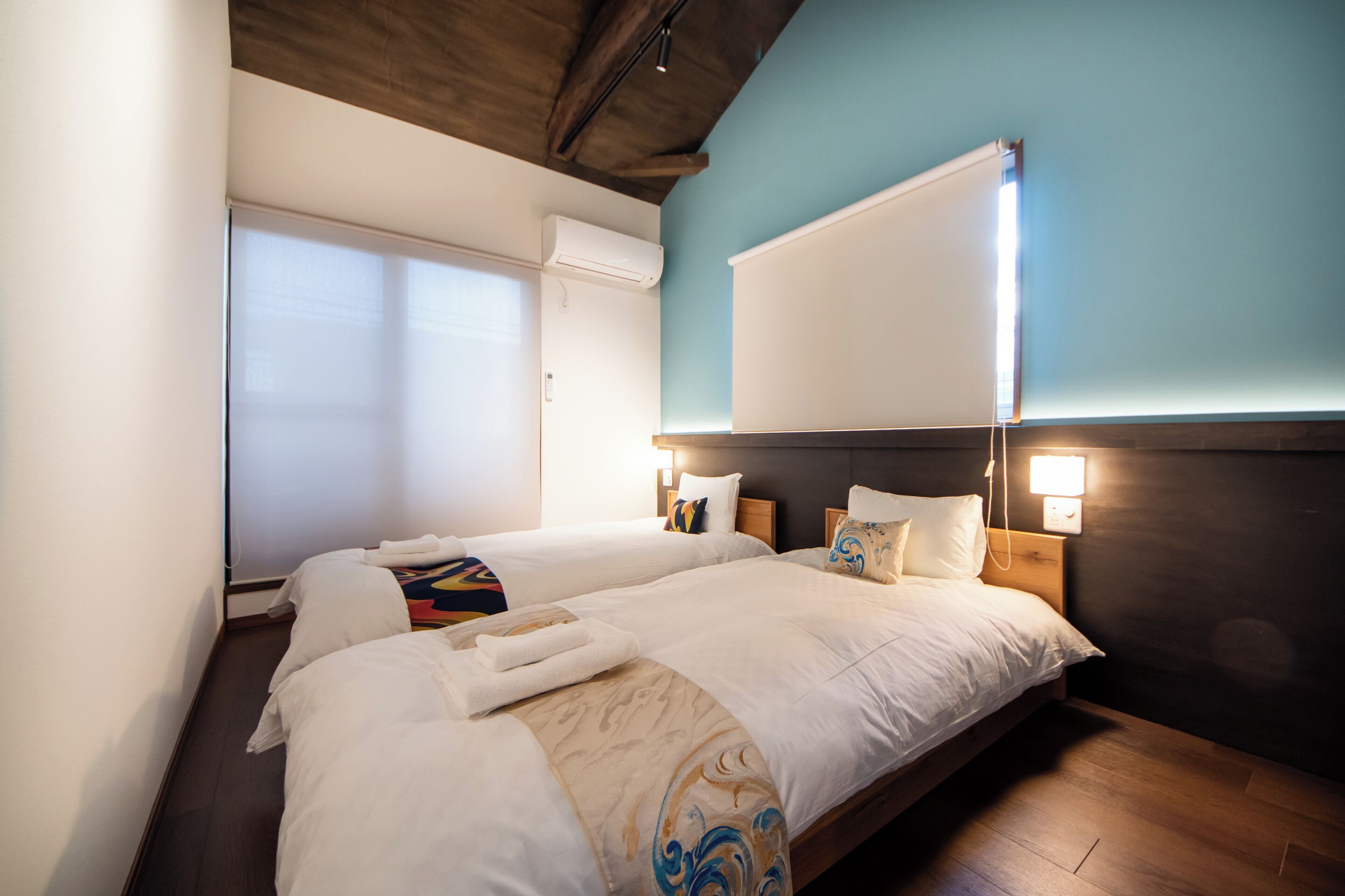 A hotel room with two beds, a large window, and a wall-mounted air conditioner.