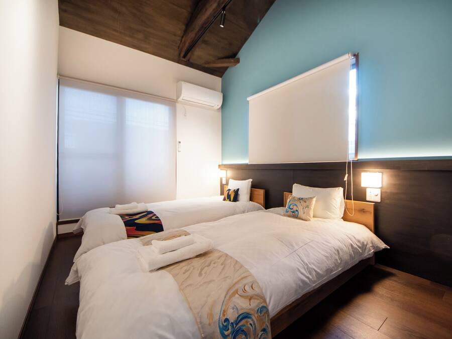 A hotel room with two beds, a large window, and a wall-mounted air conditioner.