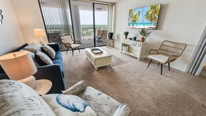 Un salon comprenant un canapé, une table basse et des fauteuils, un téléviseur fixé au mur, et un balcon avec vue.