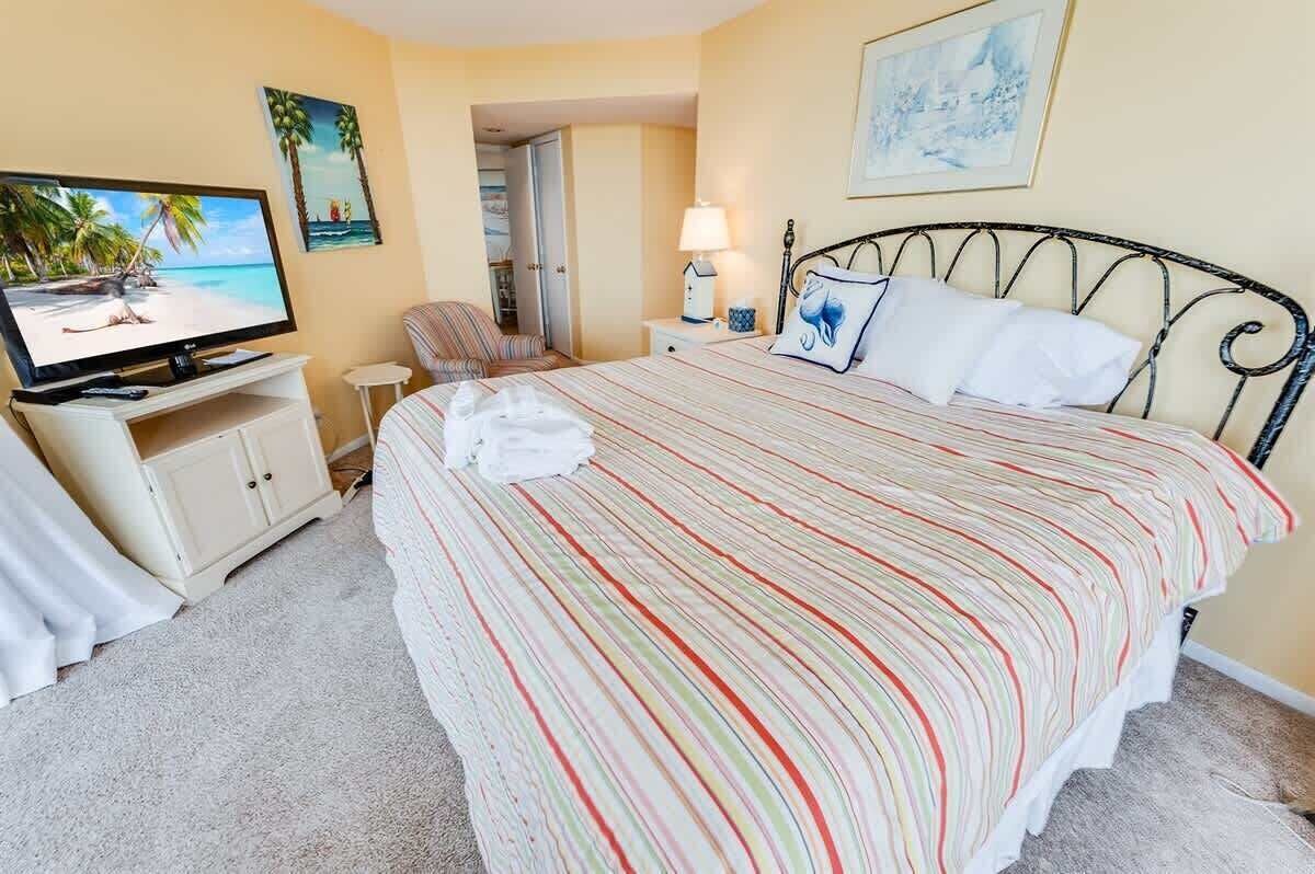 Een hotelkamer met een bed, een televisie, een stoel, een nachtkastje en een schilderij aan de muur.