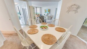 Un coin repas avec une table blanche, six chaises et des sets de table en fibres tressées.