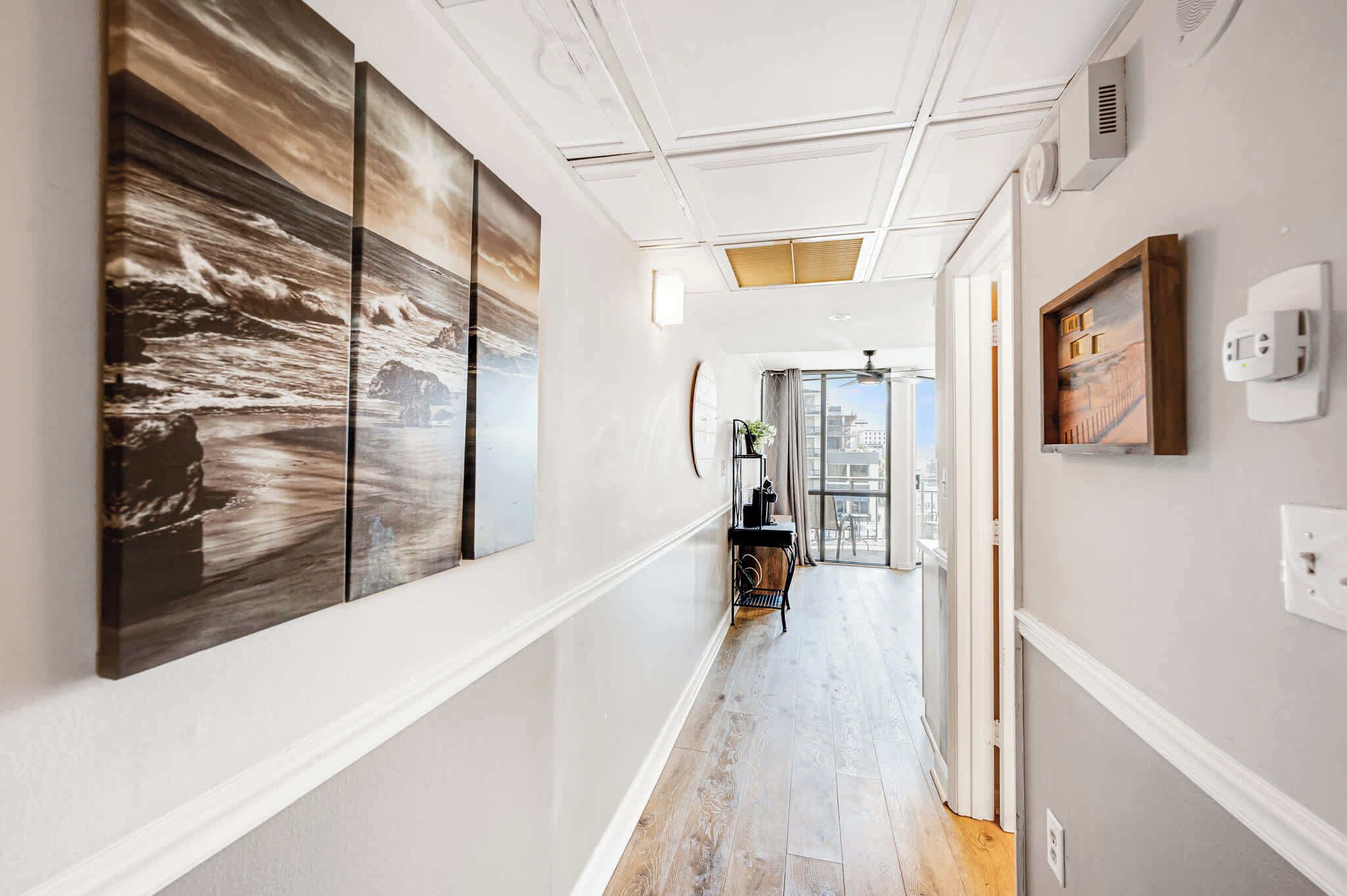 Un couloir avec une grande peinture abstraite sur le mur de gauche, une petite table avec une plante et un tableau encadré sur le mur de droite.