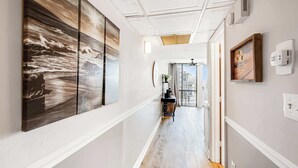 A hallway with a large abstract painting on the left, a small table with a plant, and a framed picture on the right. - Meridian Plaza 308 - 1 Bedroom (Myrtle Beach)