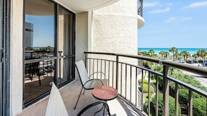 Un balcon avec une table et des chaises, une vue sur l’océan et un espace de stationnement.