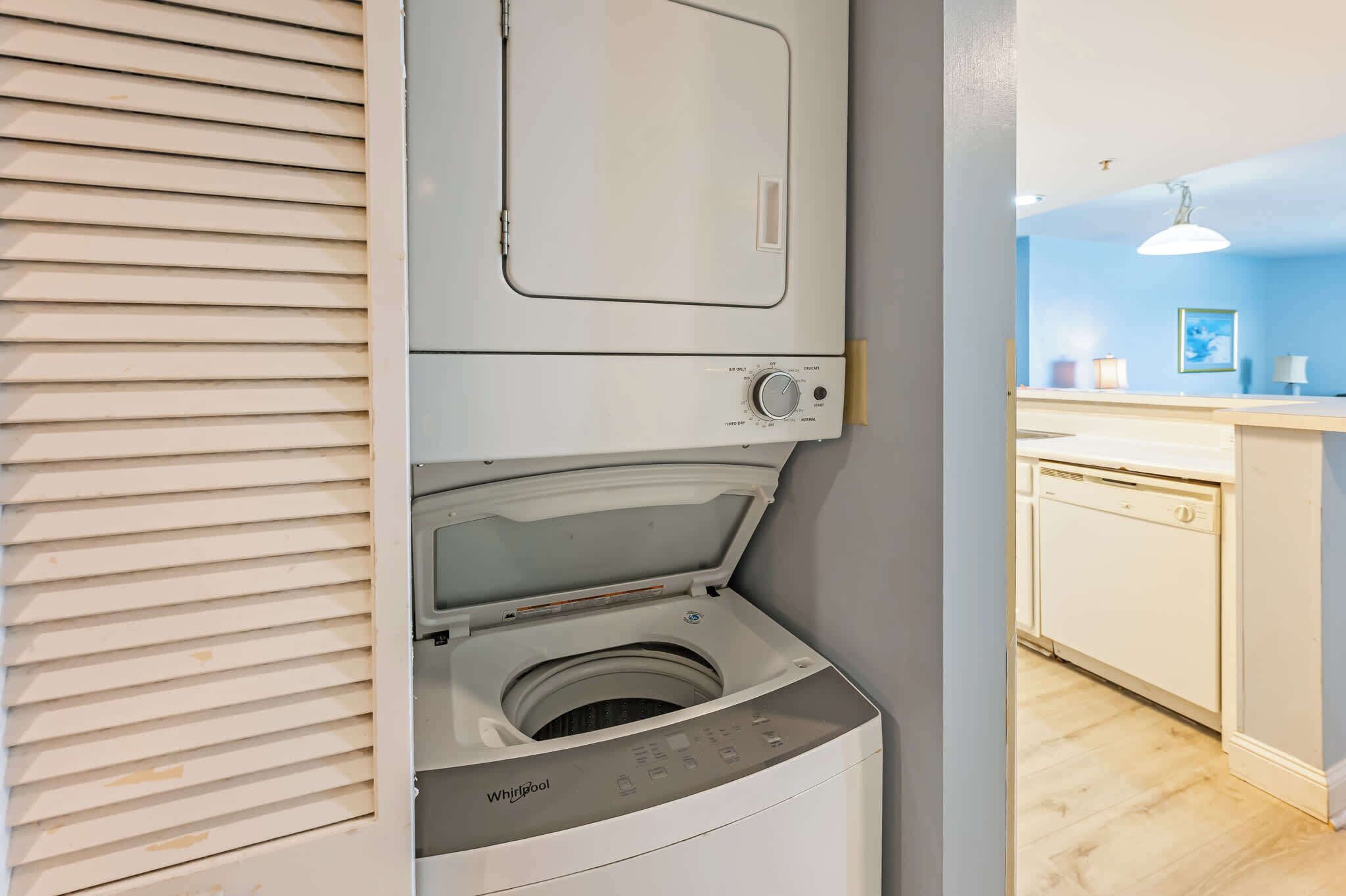 A compact laundry room with a front-loading washer and dryer, a small countertop with a sink, and a window with blinds.