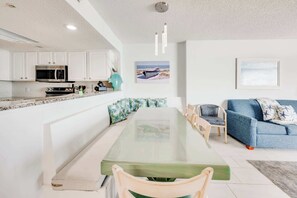 Una cocina moderna con armarios blancos, un microondas y un comedor con mesa y sillas de vidrio.