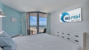 Un dormitori amb un llit gran, vistes cap a l'exterior, un rètol de 'Big Fish Rentals' i un panell de capçal blanc amb calaixos.