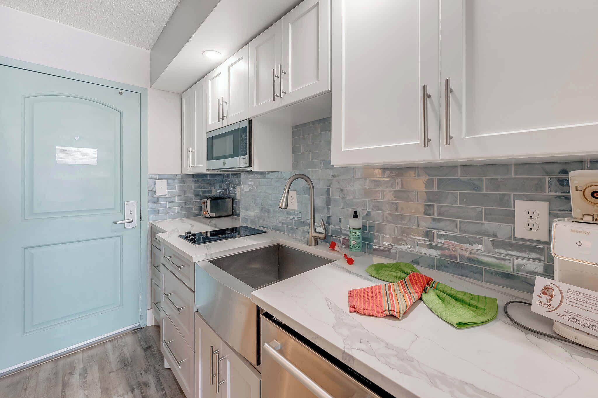 A modern kitchen with white cabinets, a stainless steel sink, a microwave, and a built-in oven.