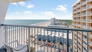 A balcony with a view of a beach and a multi-story building.