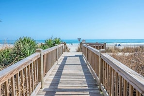 A wooden boardwalk leading to a beach with clear skies.