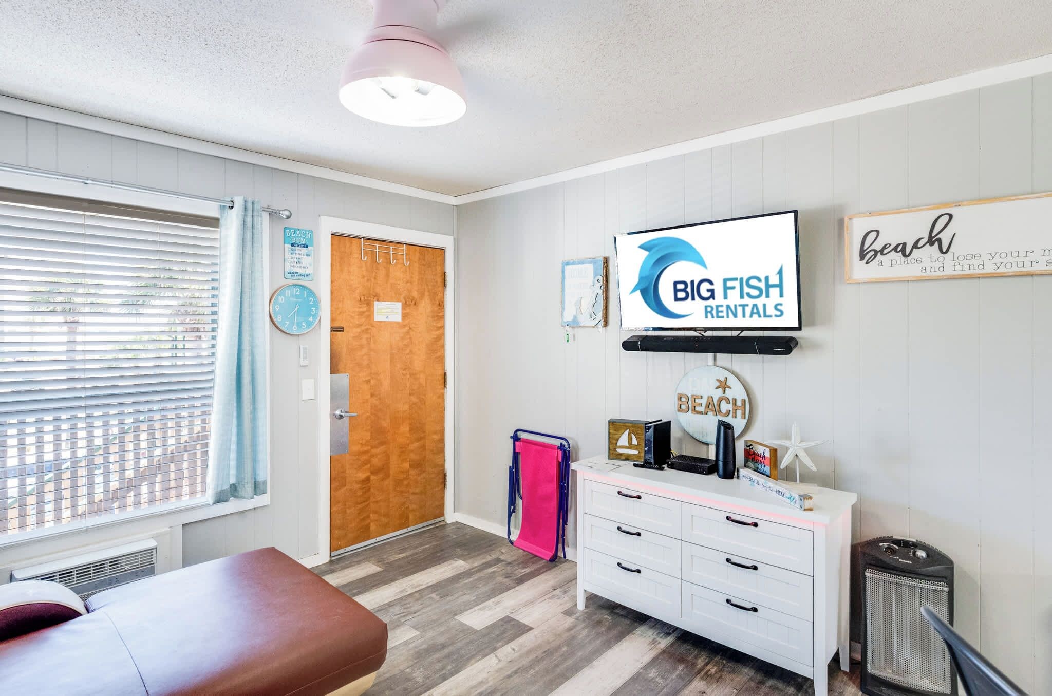 A room with a wooden door, a white dresser, a television, and a sign for Big Fish Rentals.