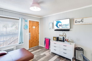 Una habitación con puerta de madera, cómoda blanca, televisor y un cartel de Big Fish Rentals.