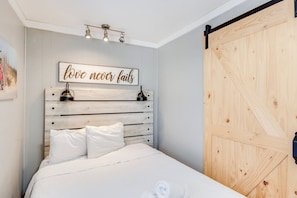 Ein Schlafzimmer mit einem hölzernen Kopfteil, einem Bett mit weißer Bettwäsche, einer Wandleuchte und einer Holztür.