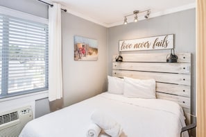 Un dormitorio con cama, lámpara de pared, un cuadro y un letrero con una frase motivacional.
