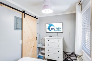 A bedroom with a sliding door, a dresser, a television displaying 'BIG FISH RENTALS', and a window with blinds. - 1BR Sea Villas in Windy Hill - Steps to the Beach! (North Myrtle Beach)