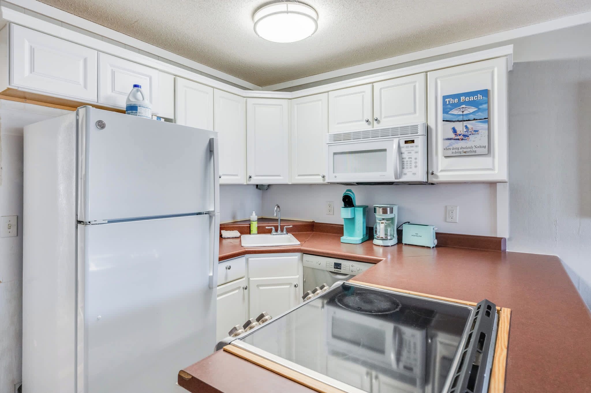 A compact kitchen with white cabinets, a refrigerator, a microwave, a sink, and a coffee maker.
