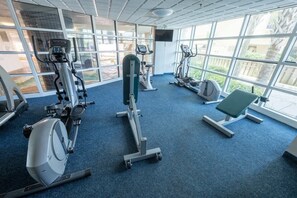 Une salle de sport équipée de machines de cardio, d’un banc et de grandes fenêtres donnant sur l’extérieur.