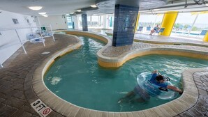 An indoor swimming pool with a 3ft depth limit, surrounded by a tiled walkway and a covered area with yellow pillars. - Coastal condo with hot tub & pools (North Myrtle Beach)