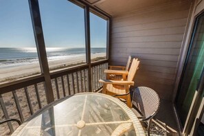 Un balcón con una mesa de vidrio y dos sillas, con vista a una playa.