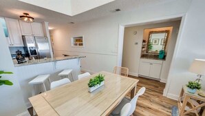 Una cocina moderna con electrodomésticos de acero inoxidable, un comedor con mesa y sillas de madera, y una pequeña isla con una planta.