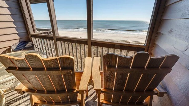 Una terraza de madera con dos sillas Adirondack mirando al mar.